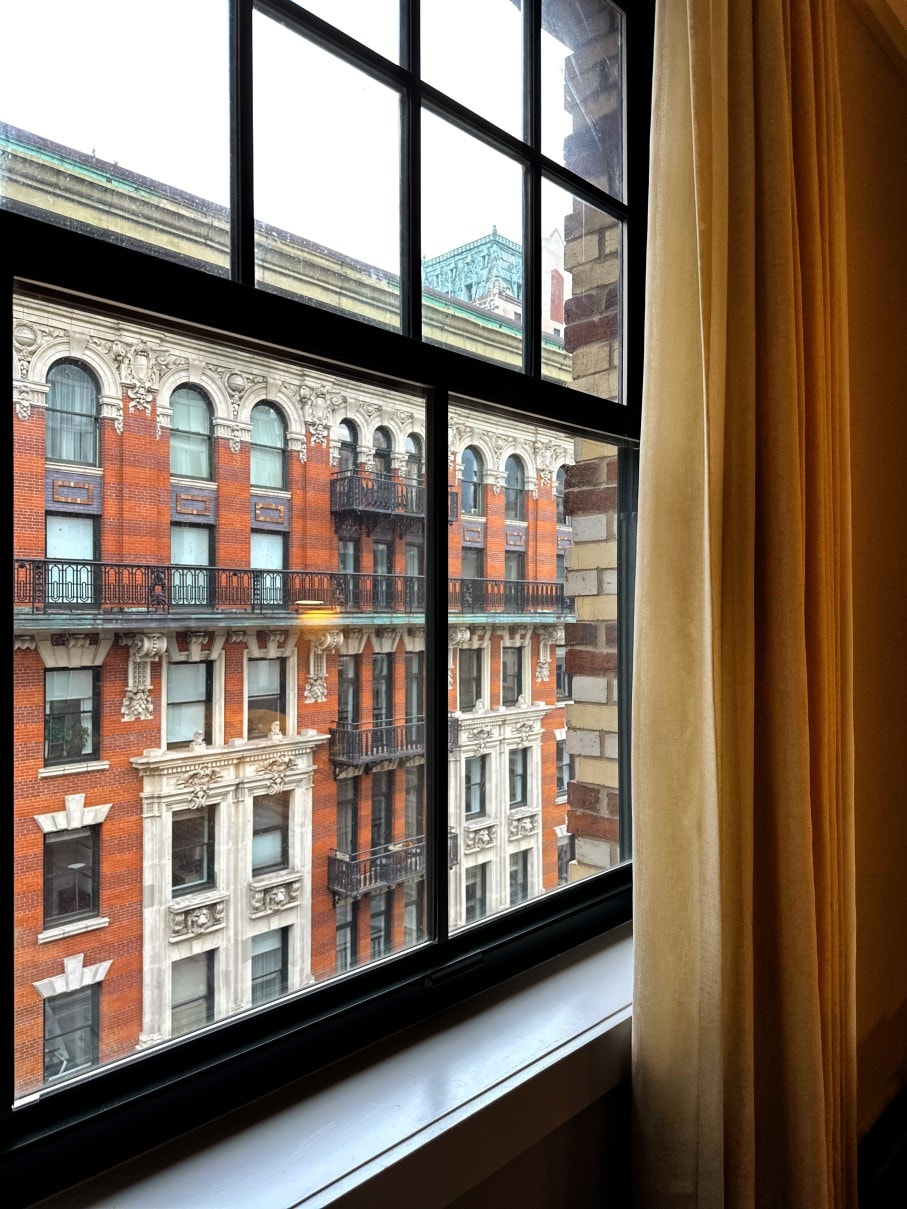 A view of a city street with brick buildings from a window with a yellow curtain.