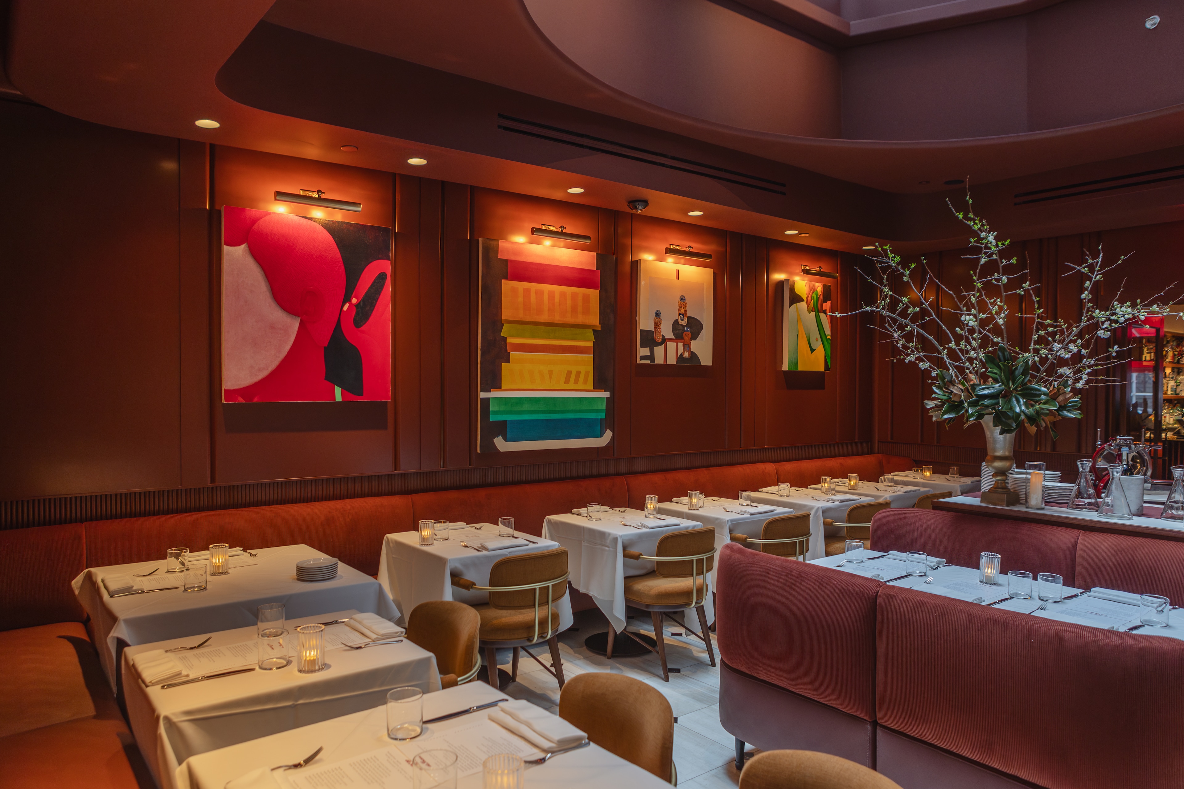 A dining room with tables set for dinner, booths, and artwork on the walls.