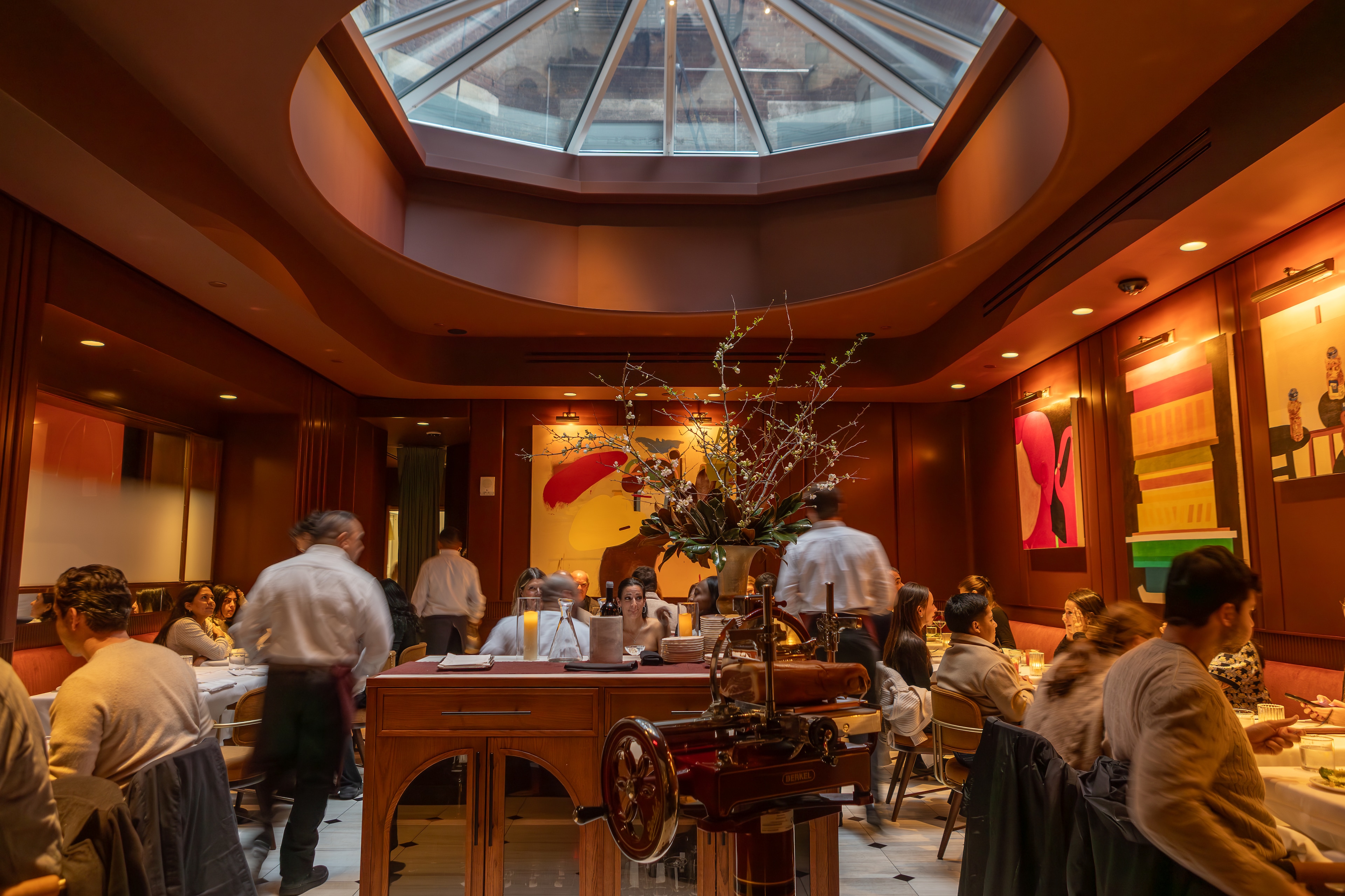 A restaurant dining area with people seated at tables, a decorative vase on a counter, and a skylight above.