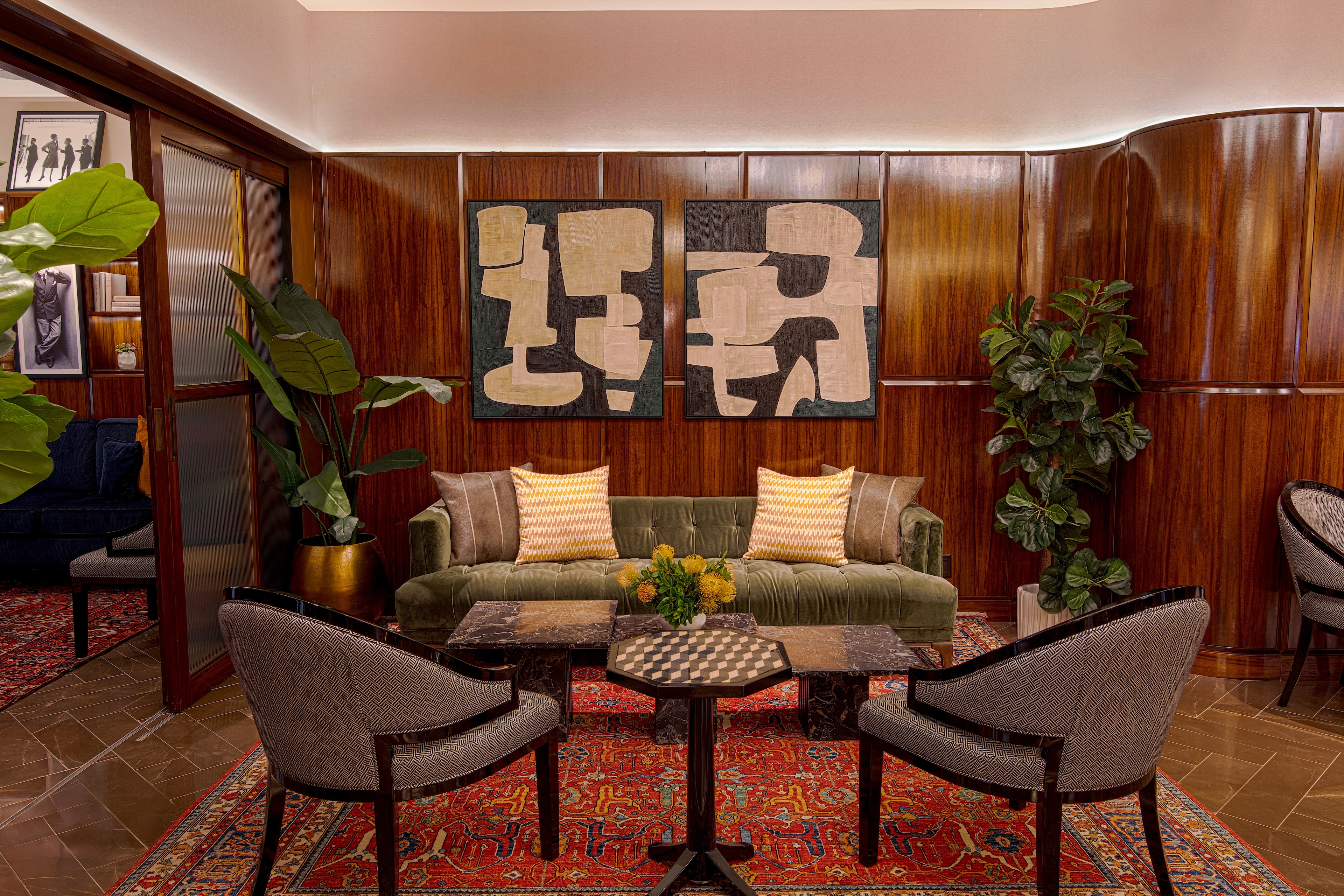 A seating area in a lobby with a green sofa, two chairs, a coffee table, and plants.