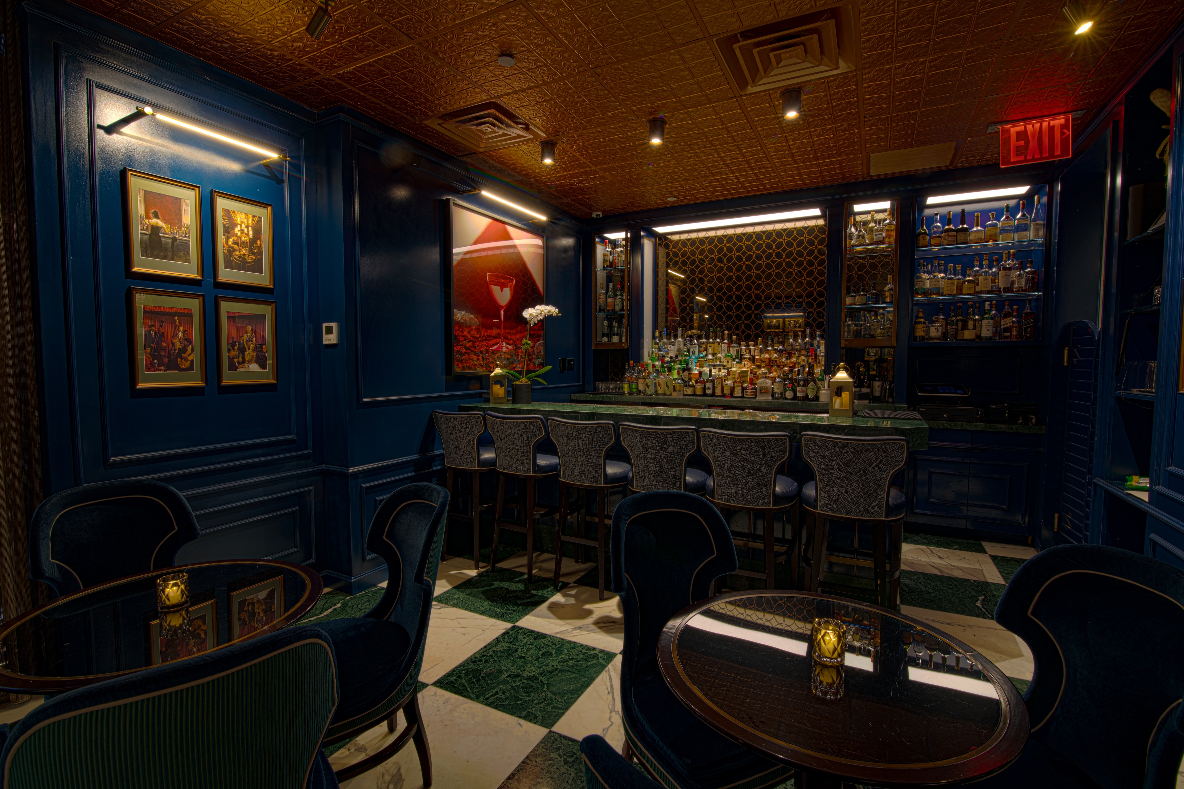 A dimly lit bar with a long counter and several high chairs, surrounded by dark blue walls and decorative elements.