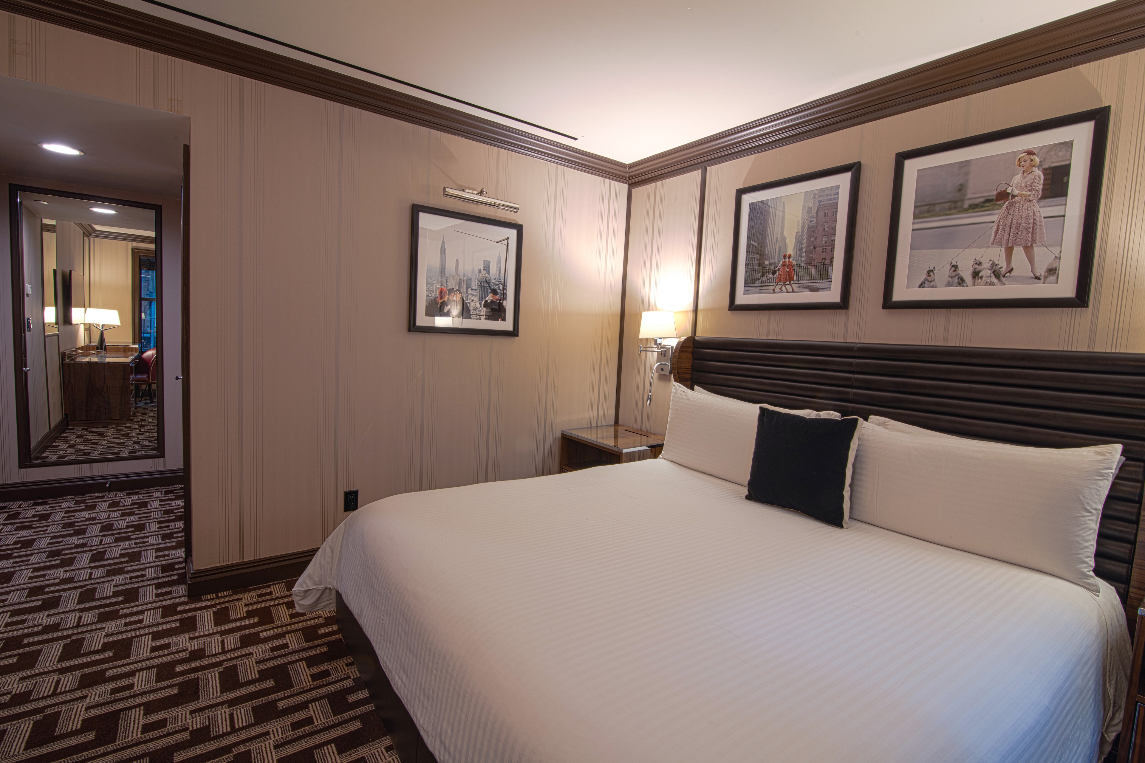 A hotel room with a large bed, a nightstand with a lamp, and framed art on the walls.