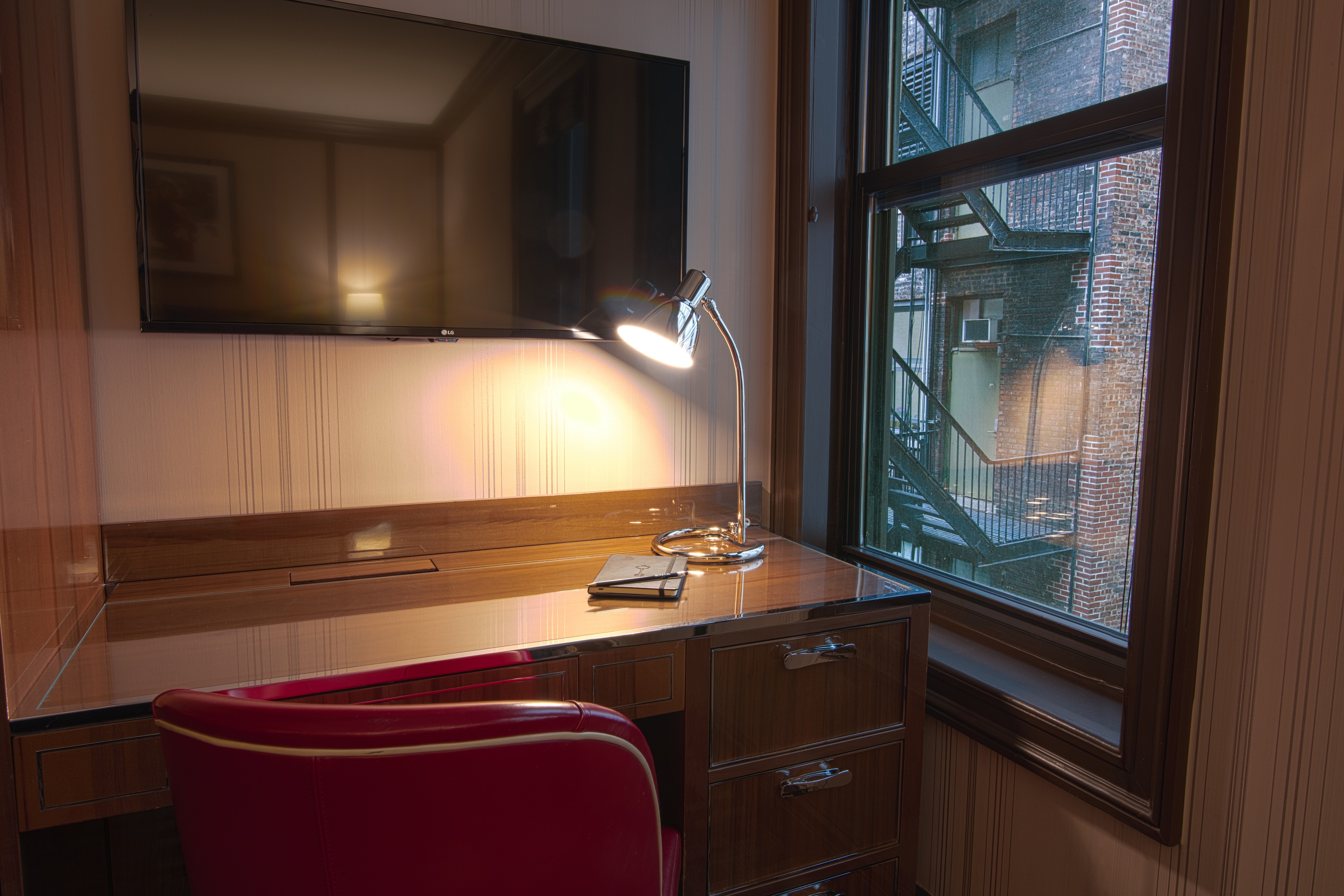 A hotel room with a desk, chair, TV, and lamp.