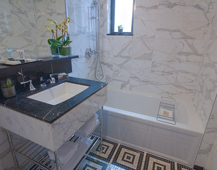A bathroom with a marble-tiled shower, a single sink vanity, and a bathtub.