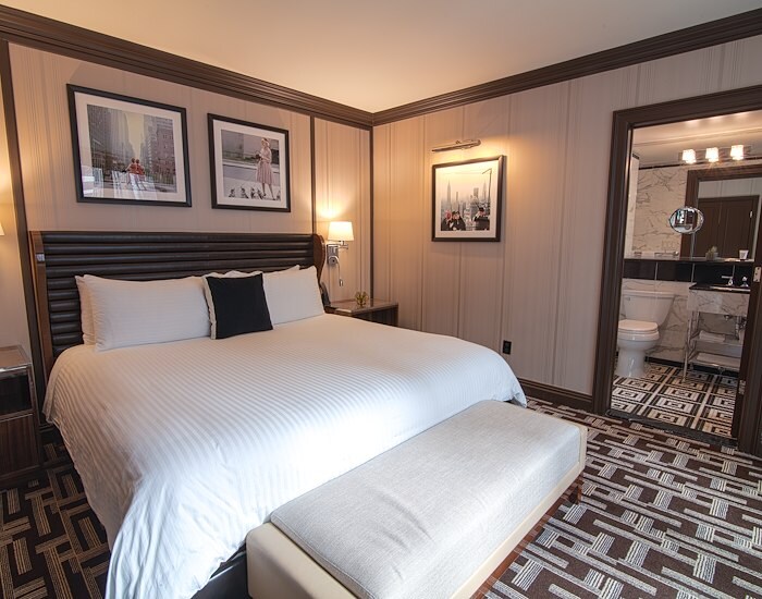 A hotel room with a large bed, bench, and pictures on the wall.