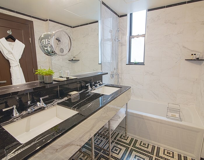 A modern bathroom with a double vanity, bathtub, and marble walls