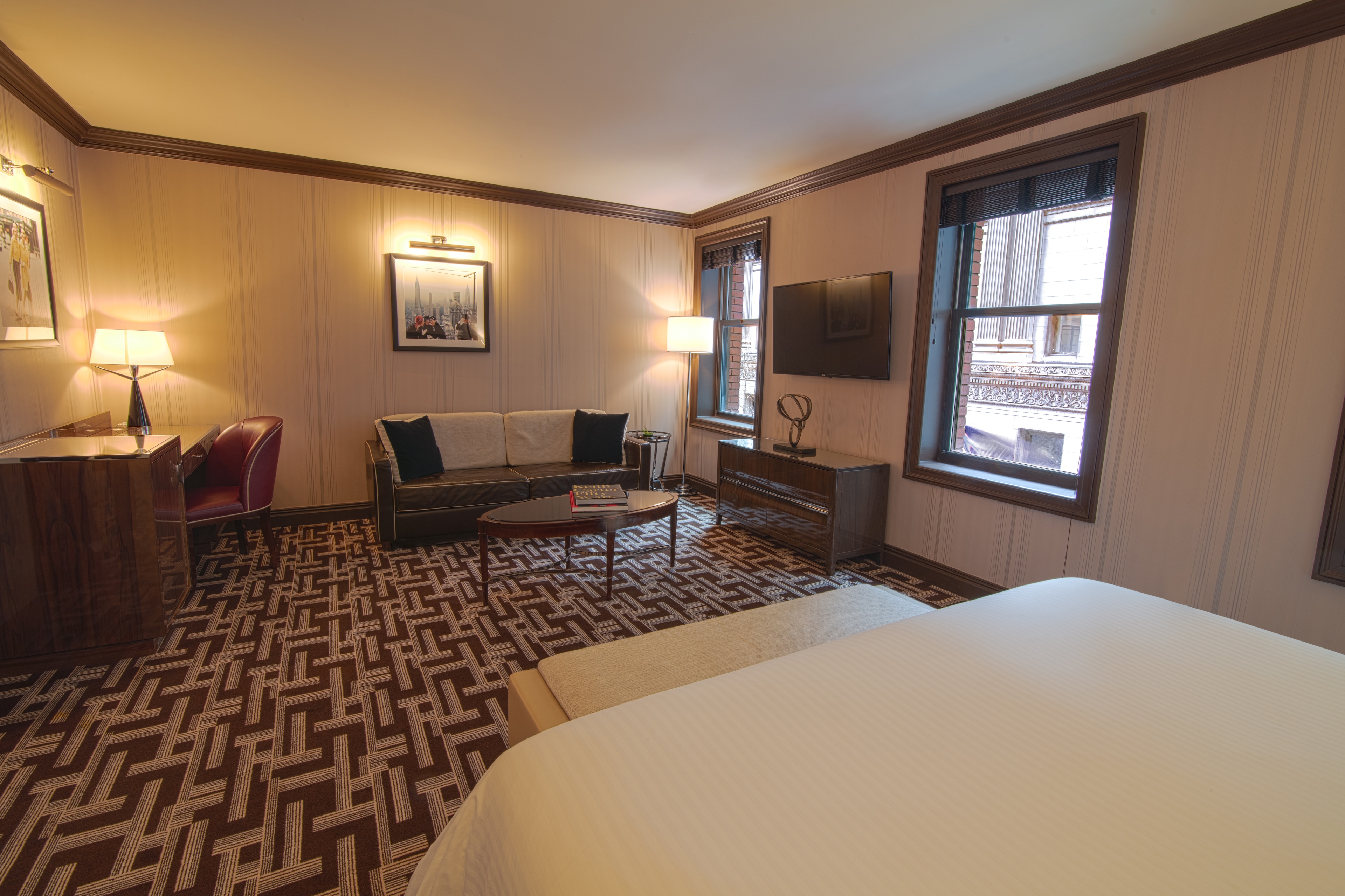 A hotel room with a bed, sofa, TV, desk, and patterned carpet.