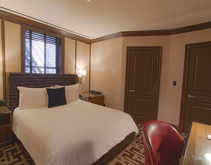 A hotel room with a king-size bed, desk, and window