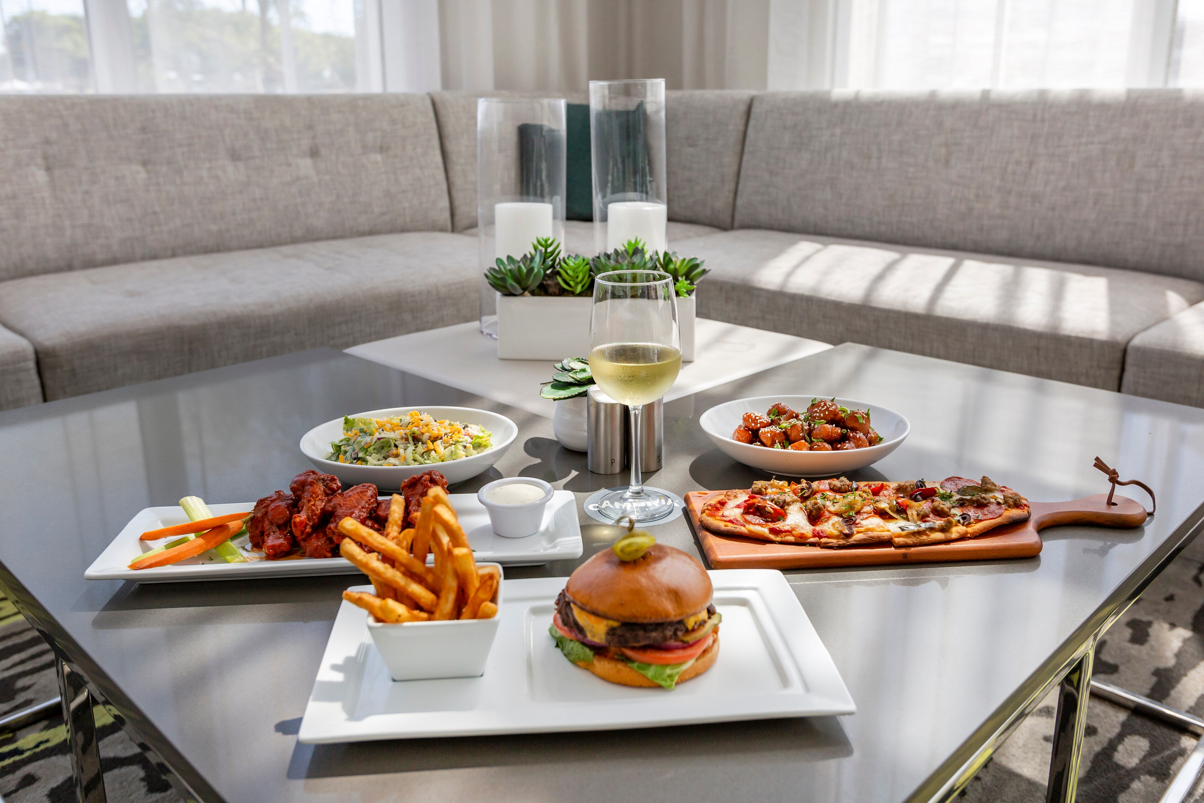 A table with a burger and fries, flatbread pizza, chicken wings, and pasta salad