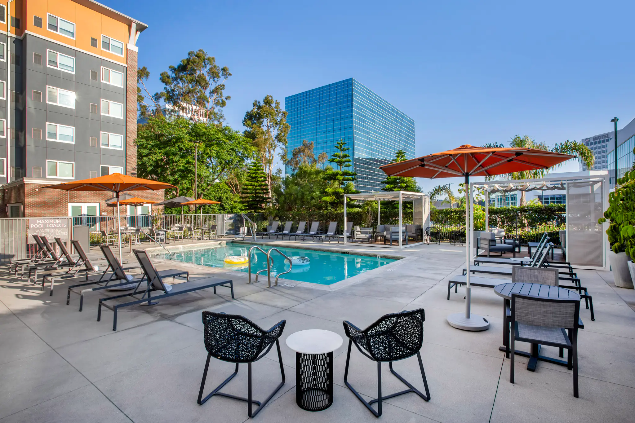 Pool area with lounge chairs, tables, and orange umbrellas under a blue sky