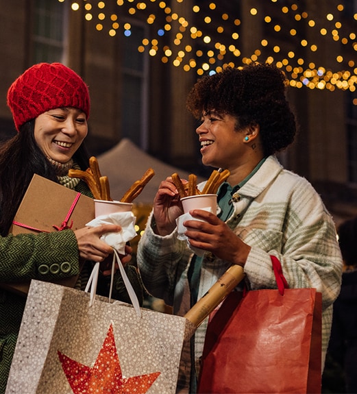 Smiling friends holding holiday shopping bags and enjoying hot chocolate and churros