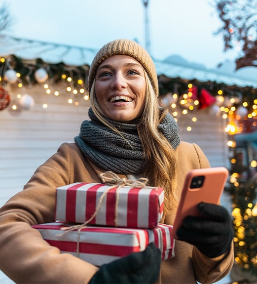 Smiling young woman looking up from her phone in front of holiday lights