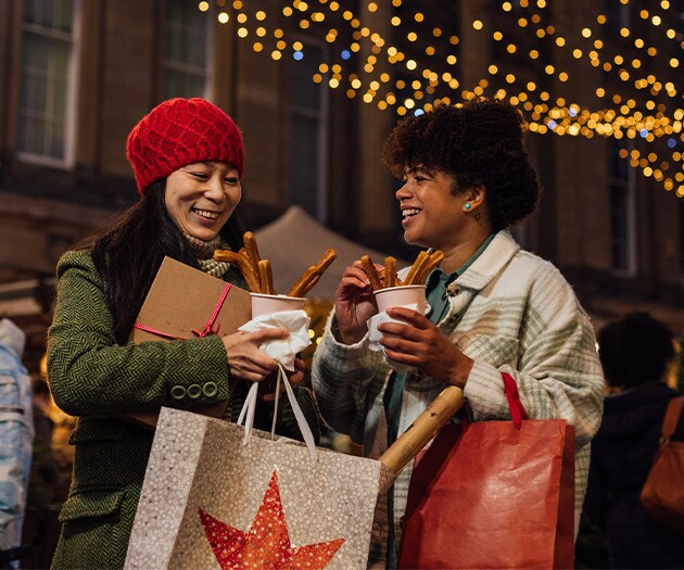 Friends holding holiday shopping bags enjoying churros and hot chocolate together