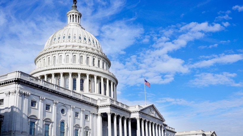 A white building with a flag on top with united states capitol in the background