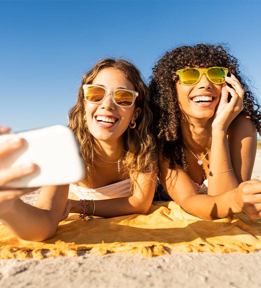 Two frinds wearing sunglasses taking a smiling selfie on the beach