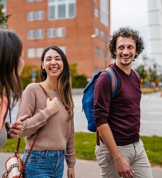 Three young adults wearing backpacks smiling and walking