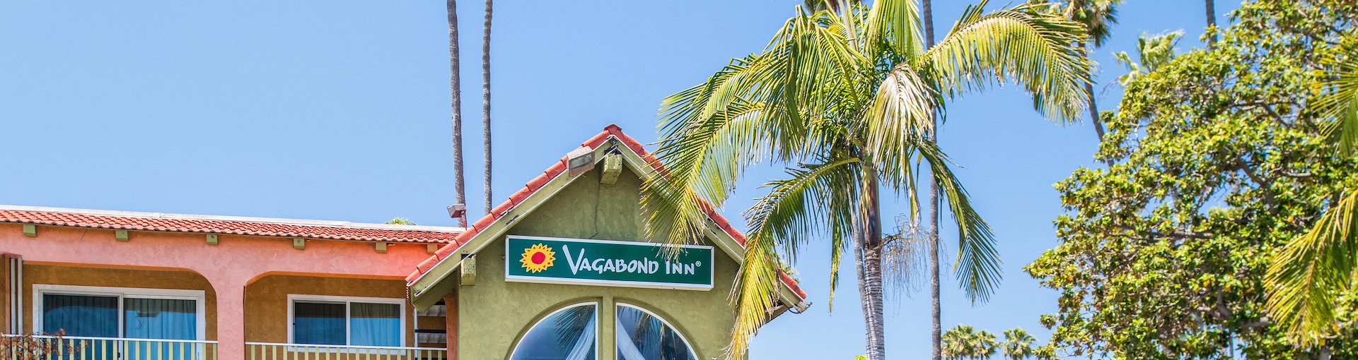 Exterior view of a hotel surrounded by palm trees, featuring a spacious parking lot in front at Vagabond Inn, California