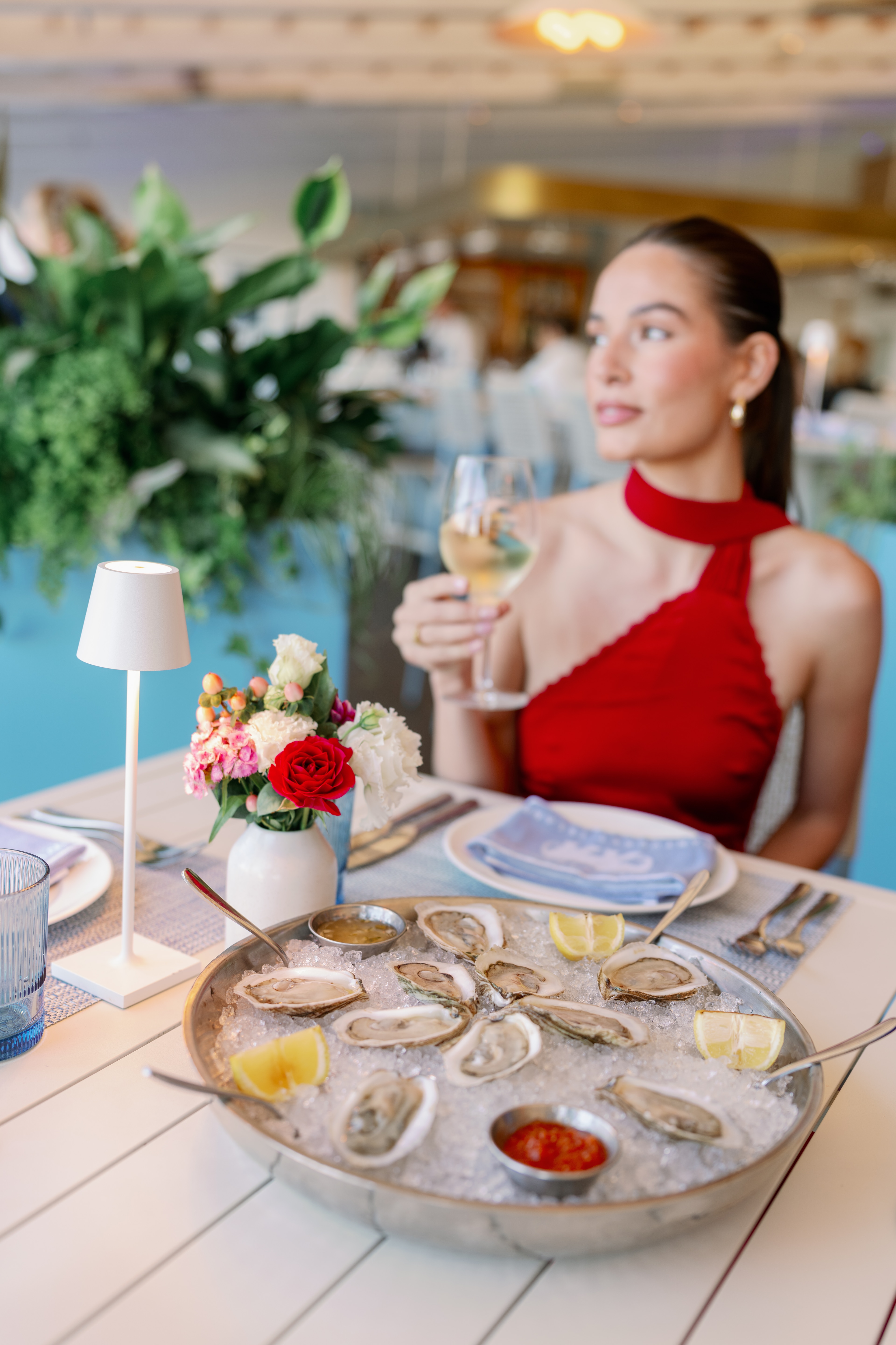 A woman in a red dress sitting at a table with oysters and wine