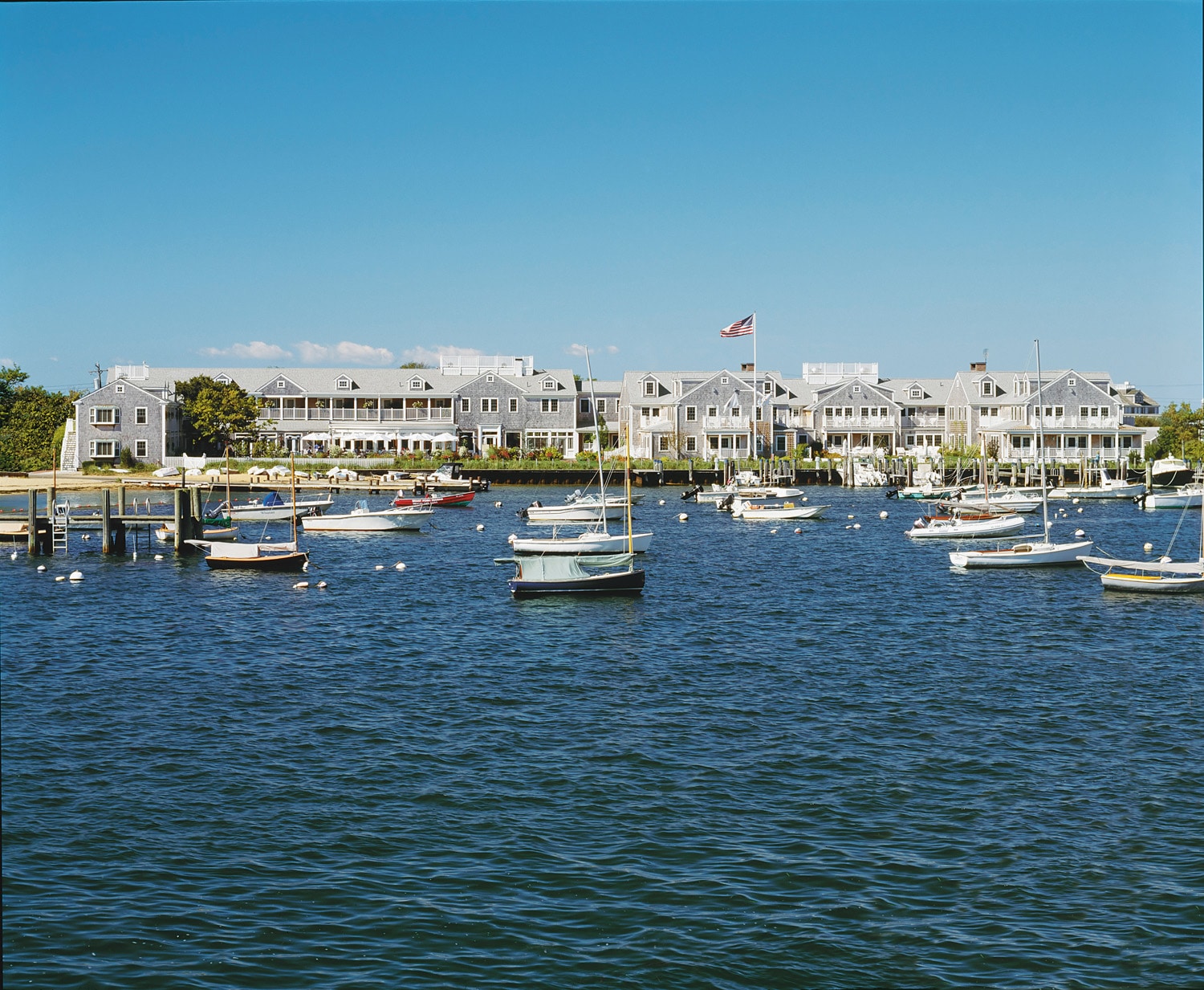 A large white building with a flag stands on the shore of a body of water with many boats.
