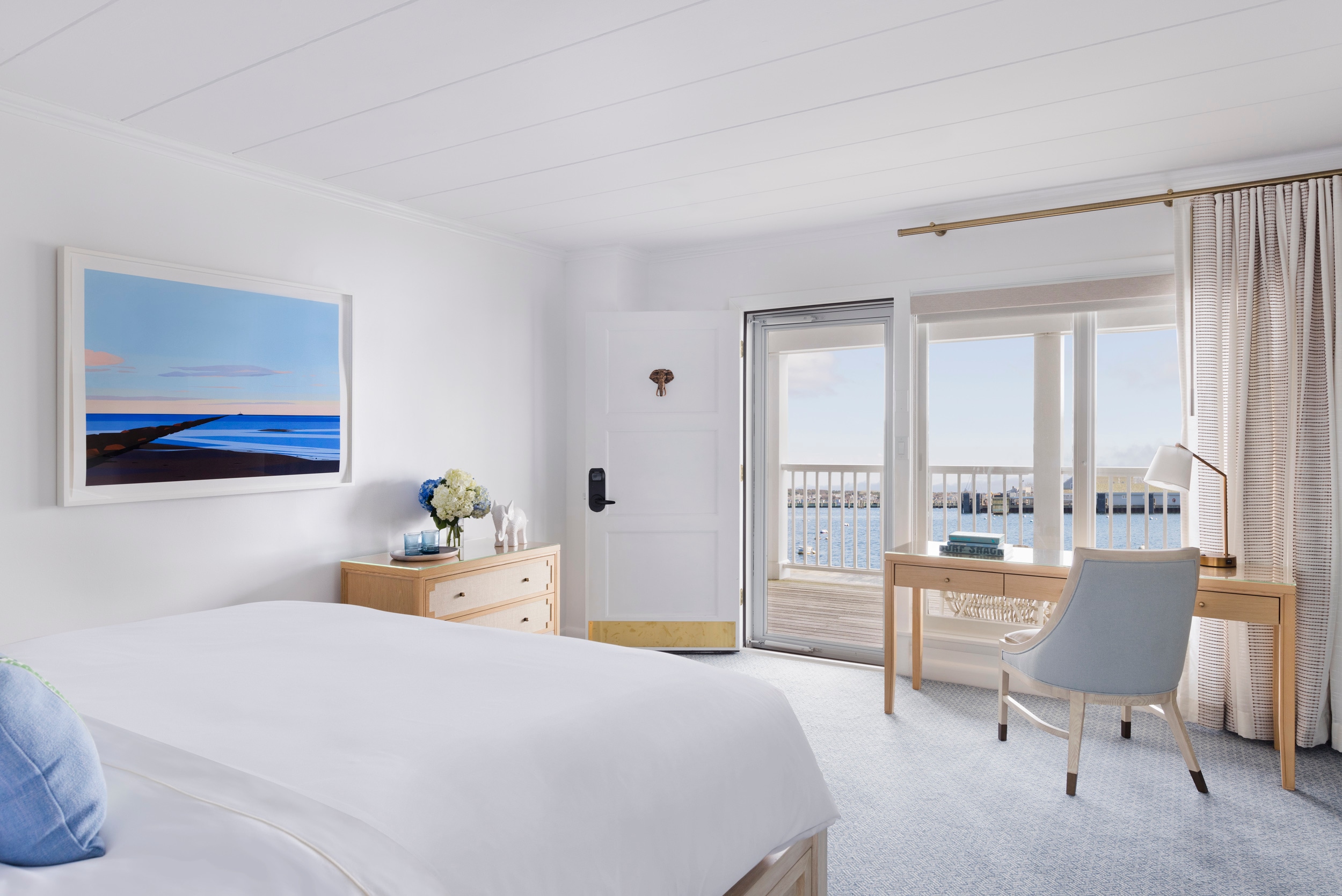 A wide view of a hotel room with a bed, desk, and balcony door.