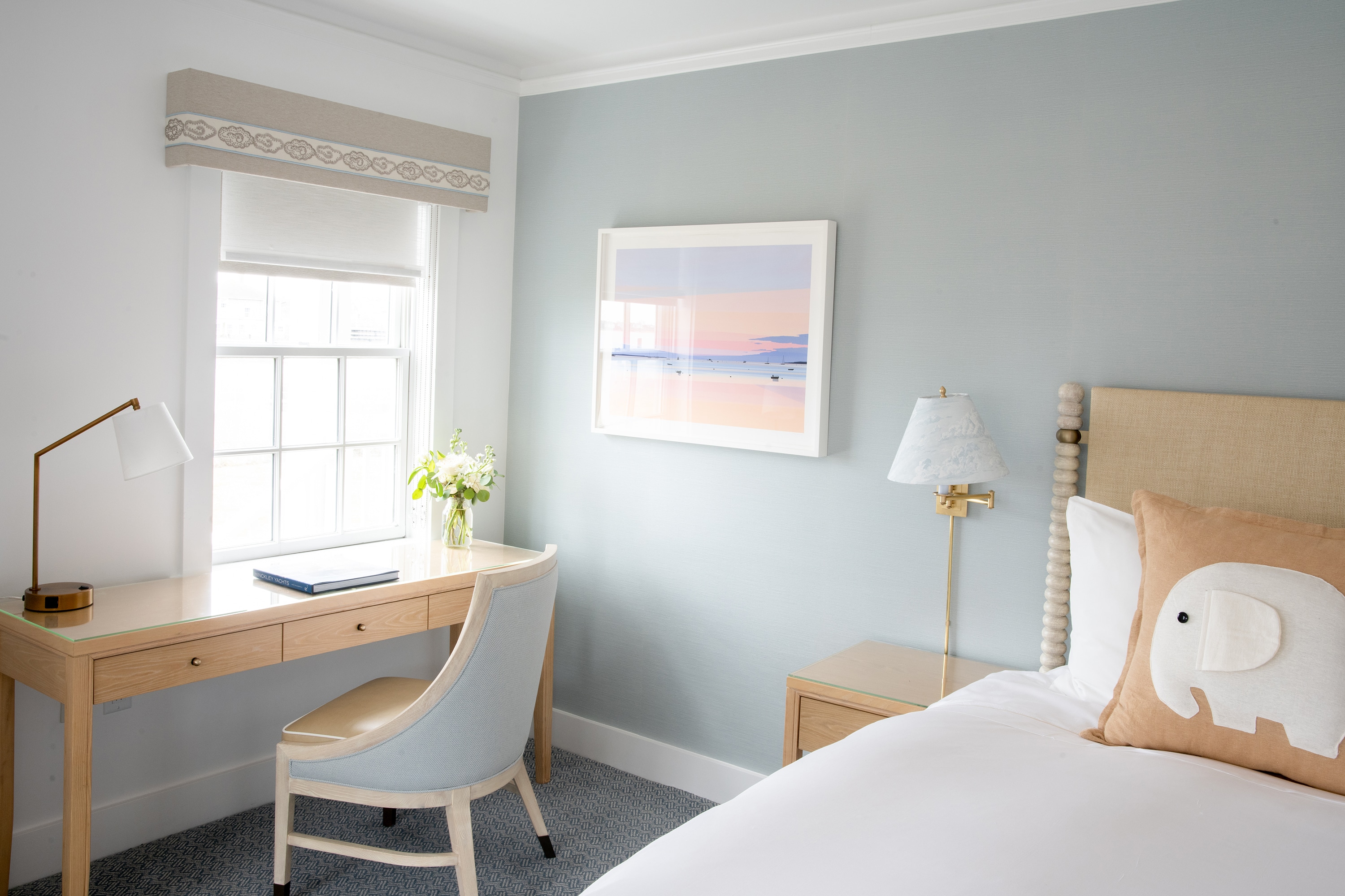 A neatly arranged hotel room with a desk, chair, bed, and artwork.