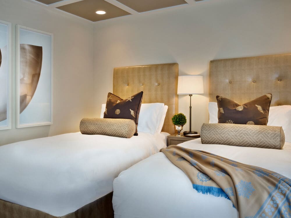 A neatly made room with two twin beds, tufted headboards, and a nightstand between them.