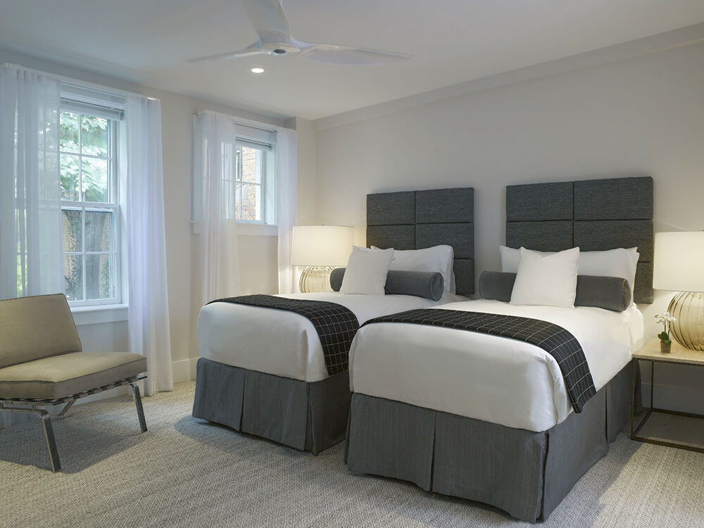 A clean and modern guest room with twin beds, a chair, and a ceiling fan.