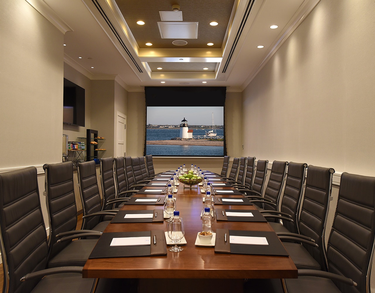 a long meeting room table with leather chairs, a projector screen, and a view of a lighthouse
