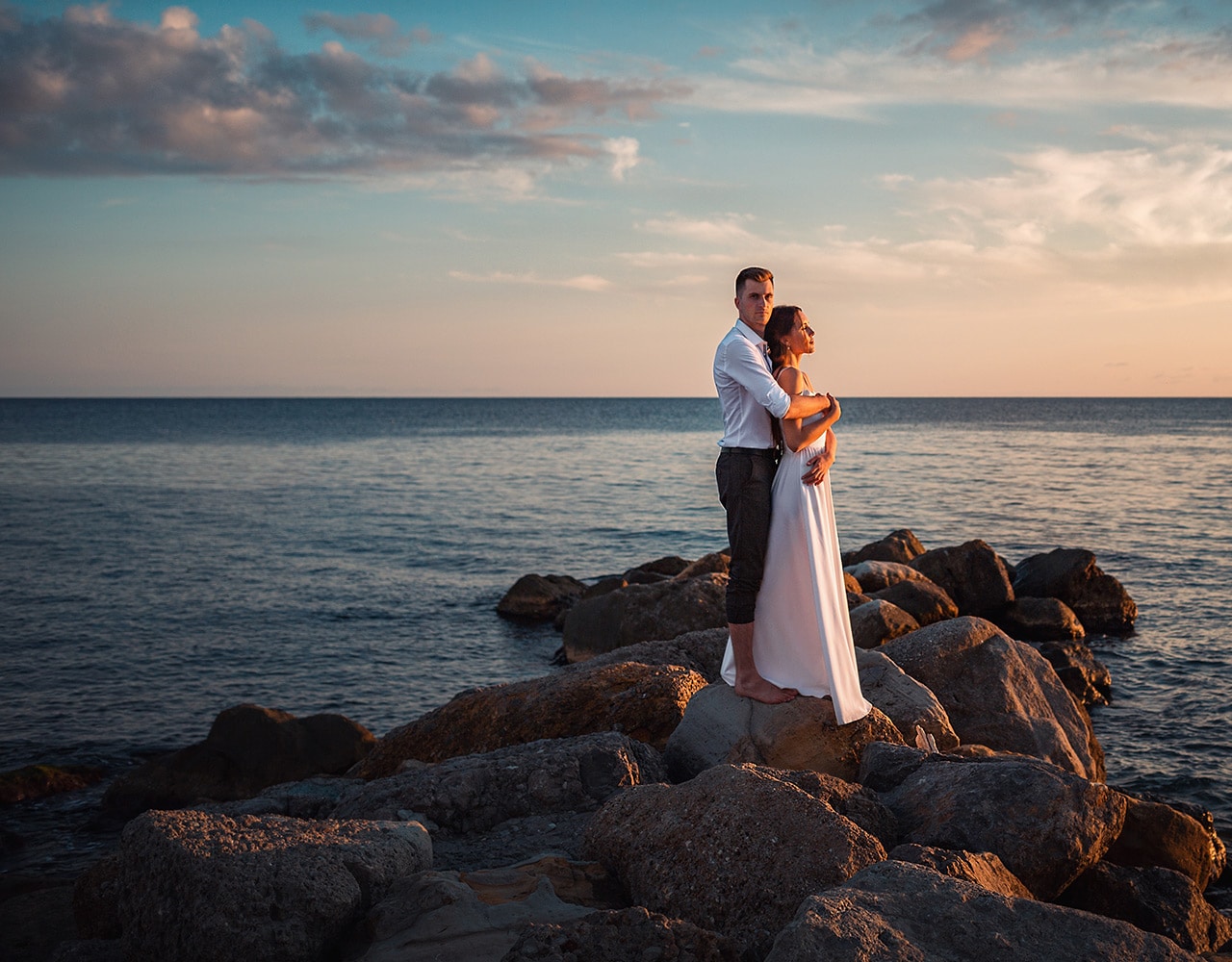 A couple embracing on rocks by the ocean during sunset