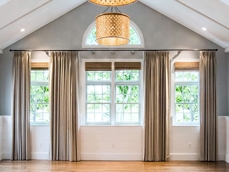 A bright and airy room with a vaulted ceiling, large windows, and a chandelier.