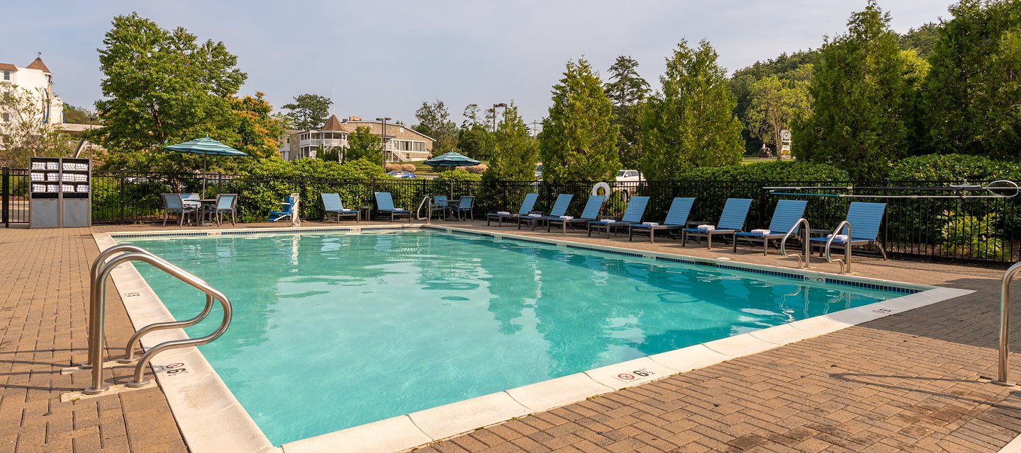 Outdoor pool surrounded by blue lounge chairs and green trees under a clear sky