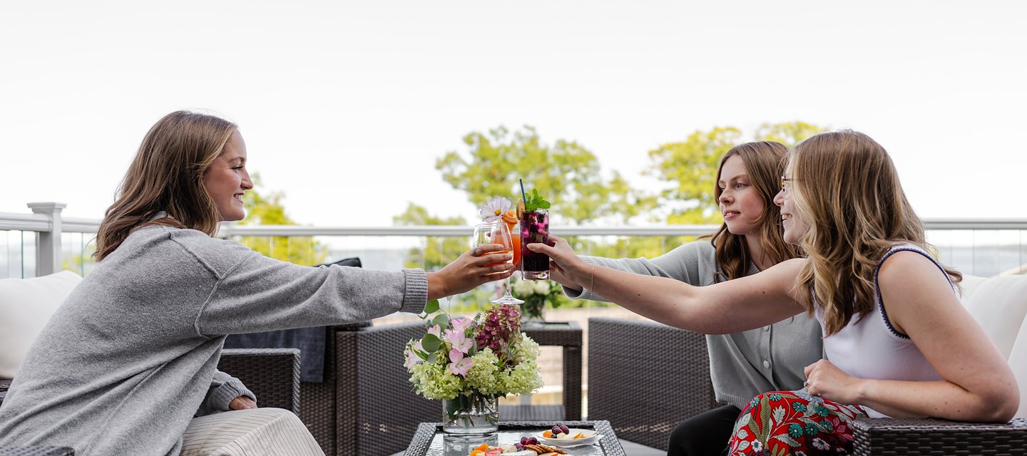 Three Women Sit on a Patio Raising Glasses in a Toast