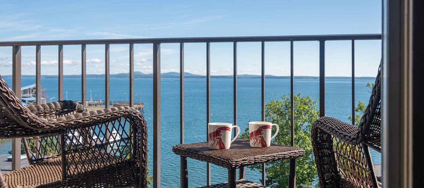 Two wicker chairs and a table with two mugs on a balcony