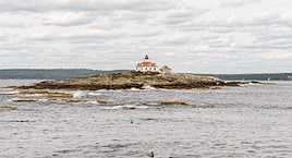 A small coastal island with a lighthouse and a house, surrounded by rocky shores