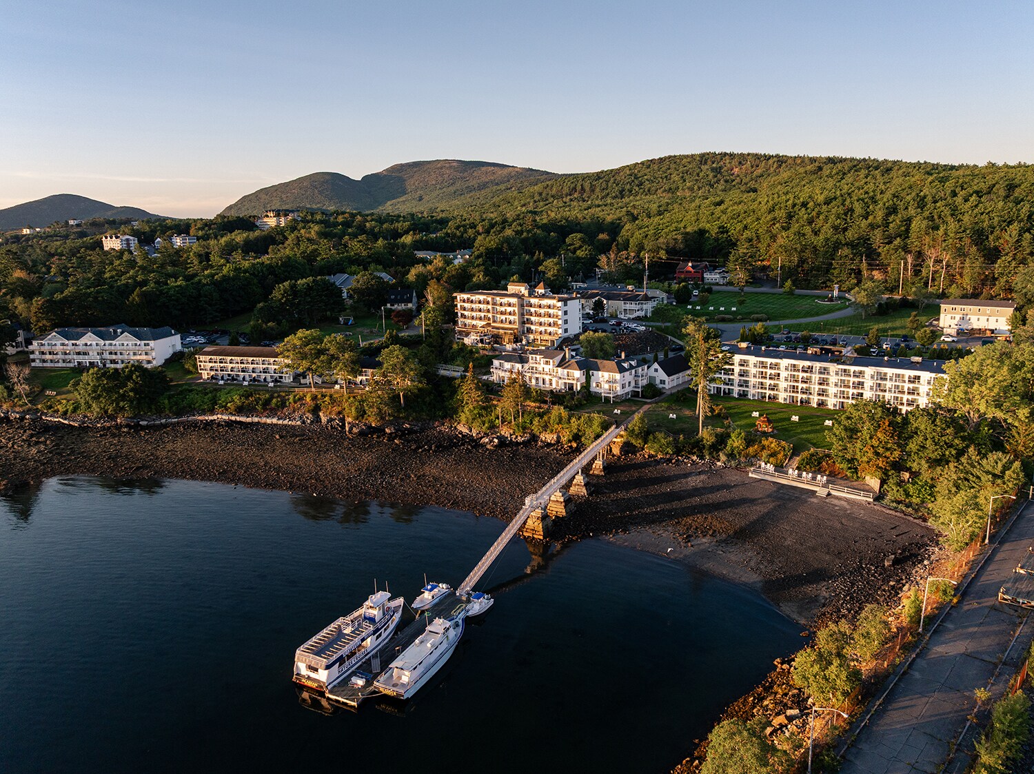 Aerial view of a coastal town at sunset, featuring docked boats by a pier
