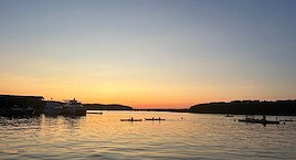 Sunset over a calm harbor with silhouetted kayakers on the water