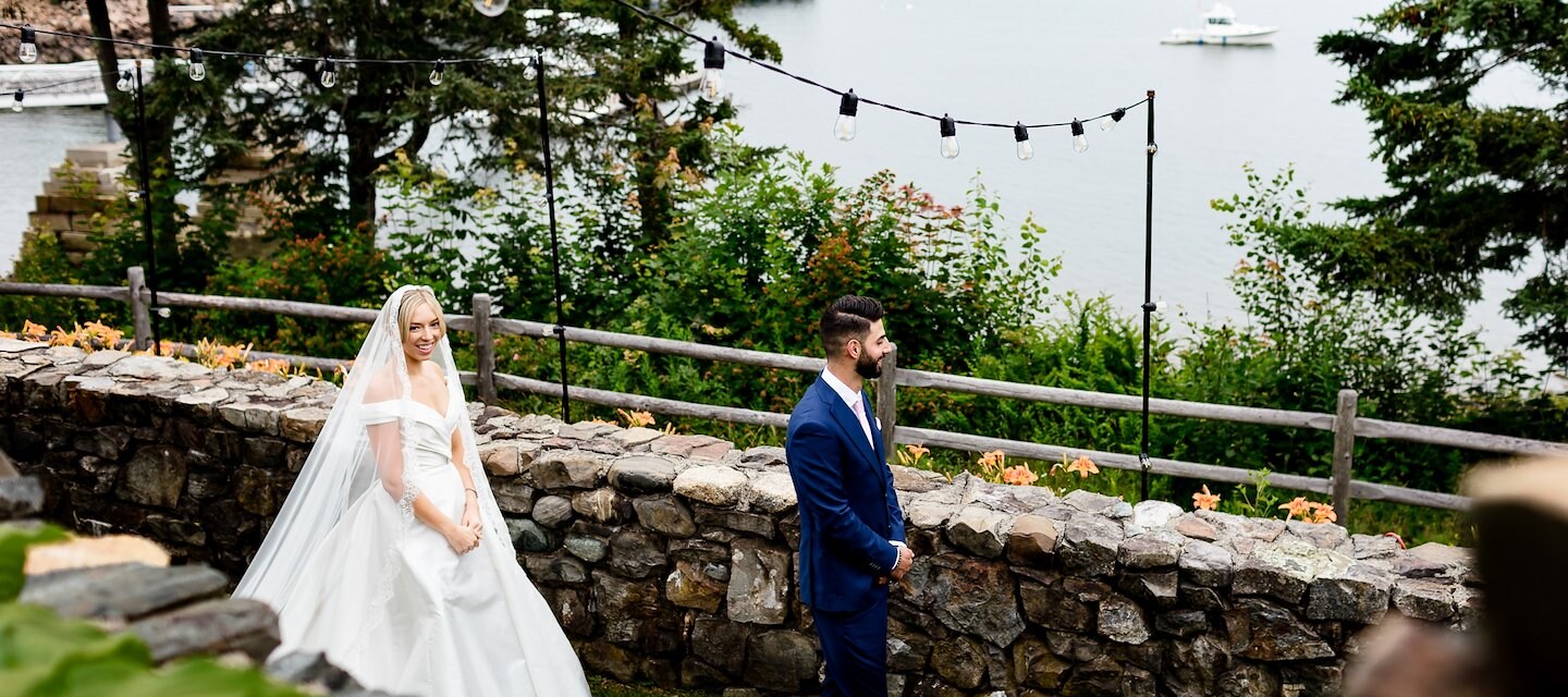 Bride and groom walk through the garden by a rock wall outside the Atlantic Oceanside Hotel