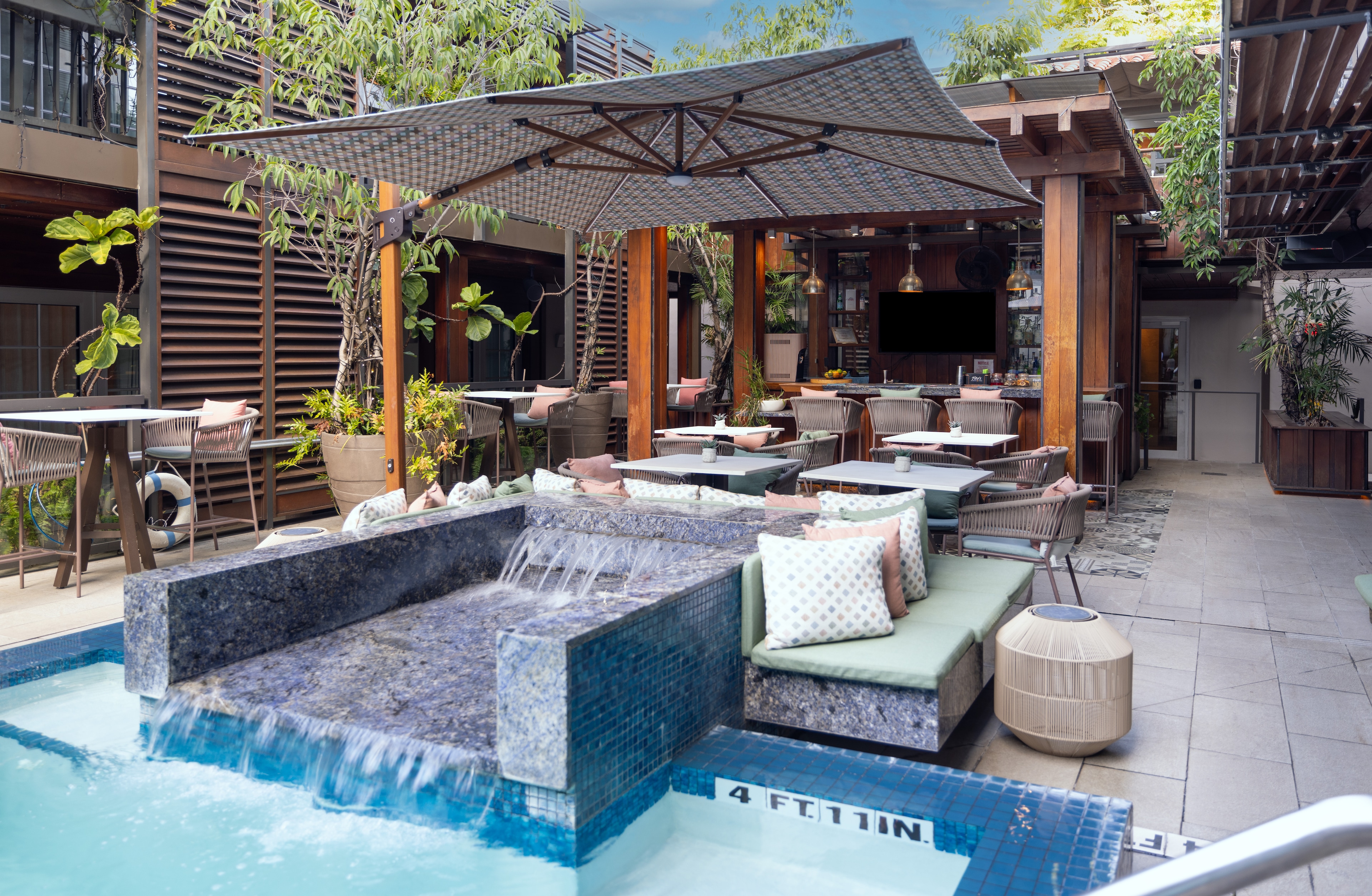 A poolside area with a waterfall, seating, and umbrellas.