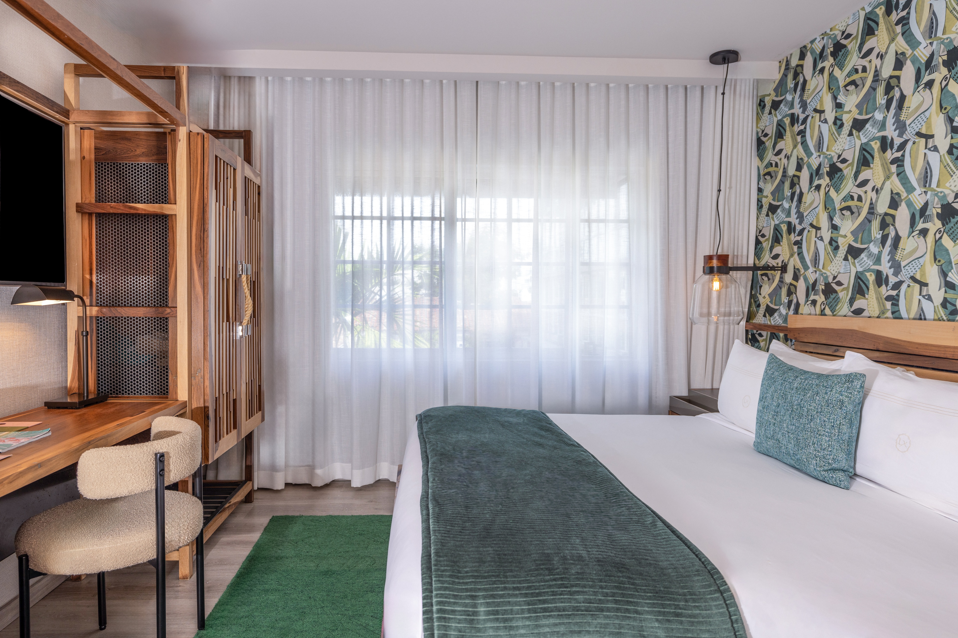 A hotel room with a bed, desk, and window.
