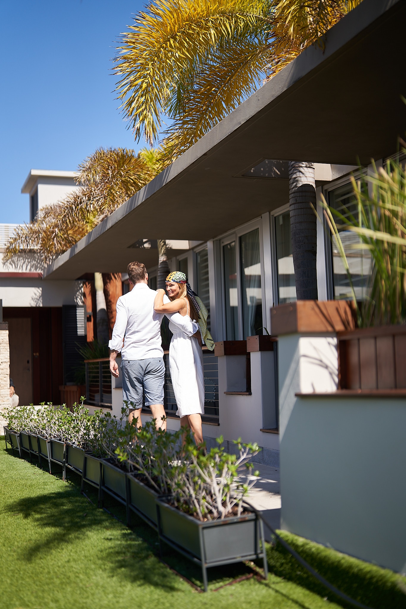 A couple walking towards the entrance of a modern building with a covered porch and large windows.