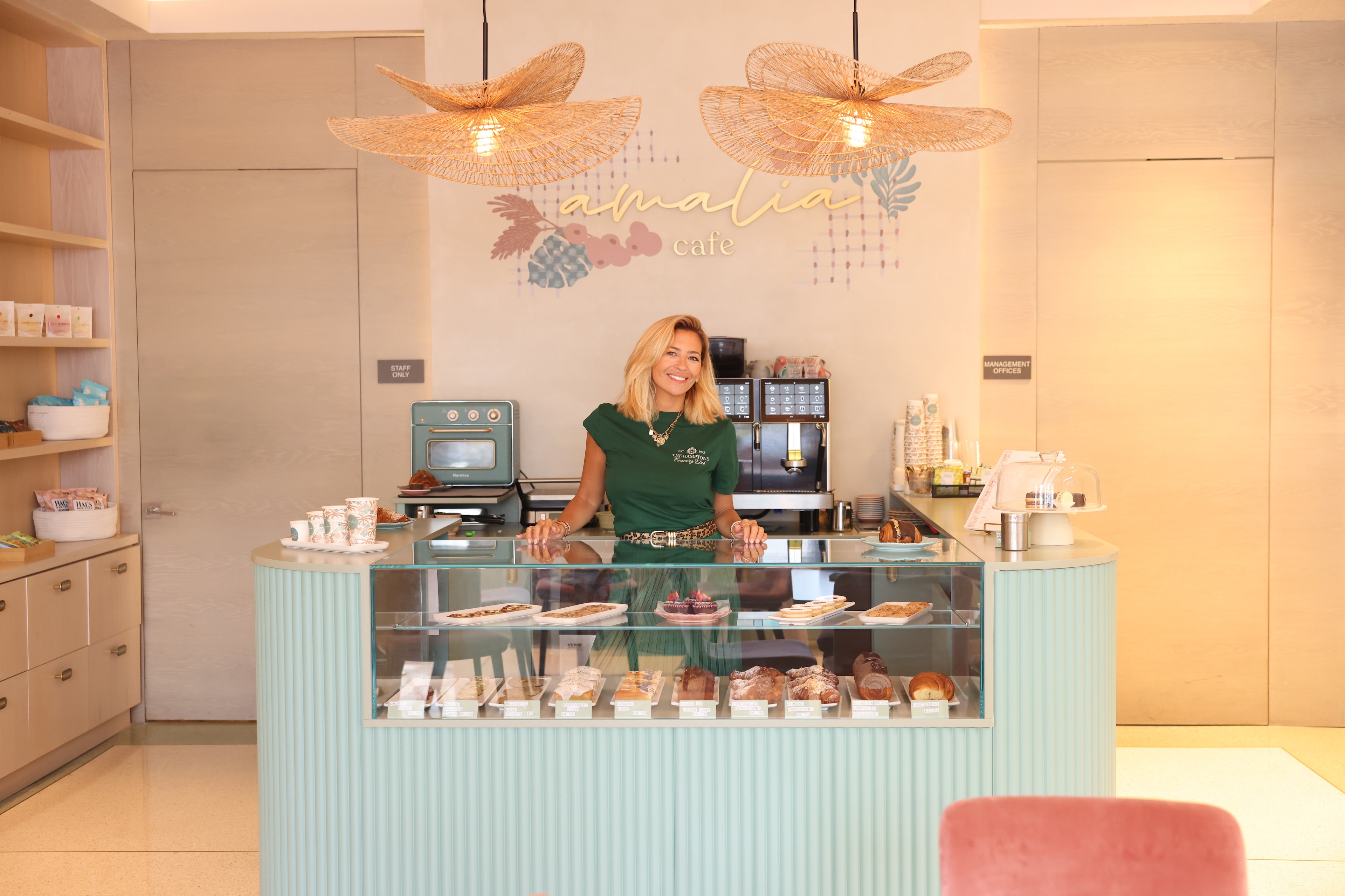 A woman stands behind a counter with pastries and drinks on display.