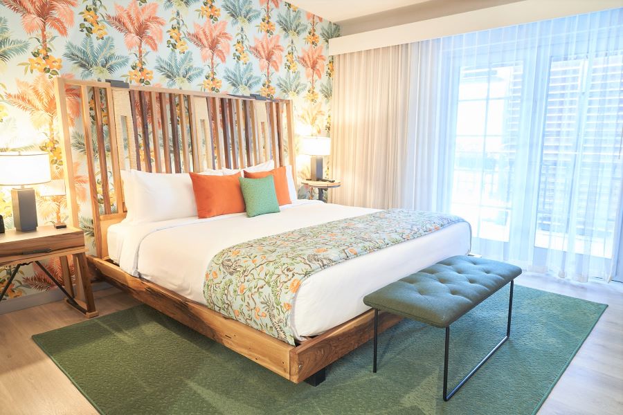 A hotel room with a large bed, floral wallpaper, and a window with sheer curtains.