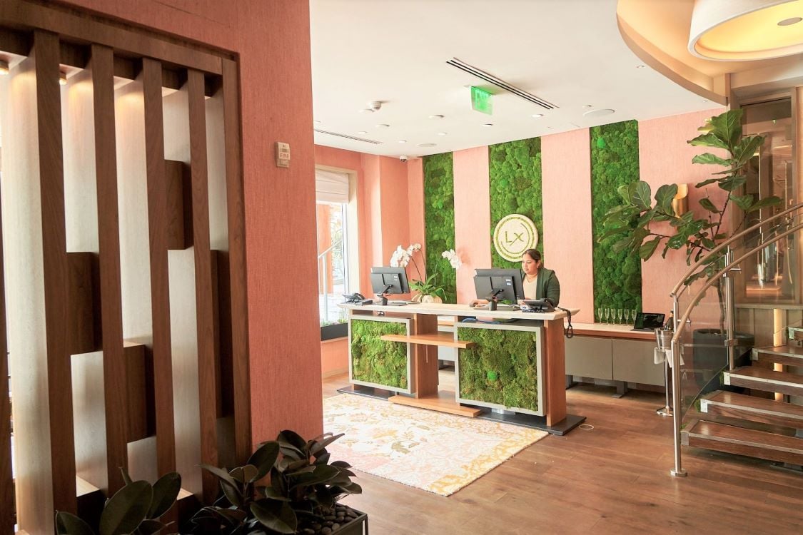 A hotel lobby with a reception desk, plants, and a staircase.