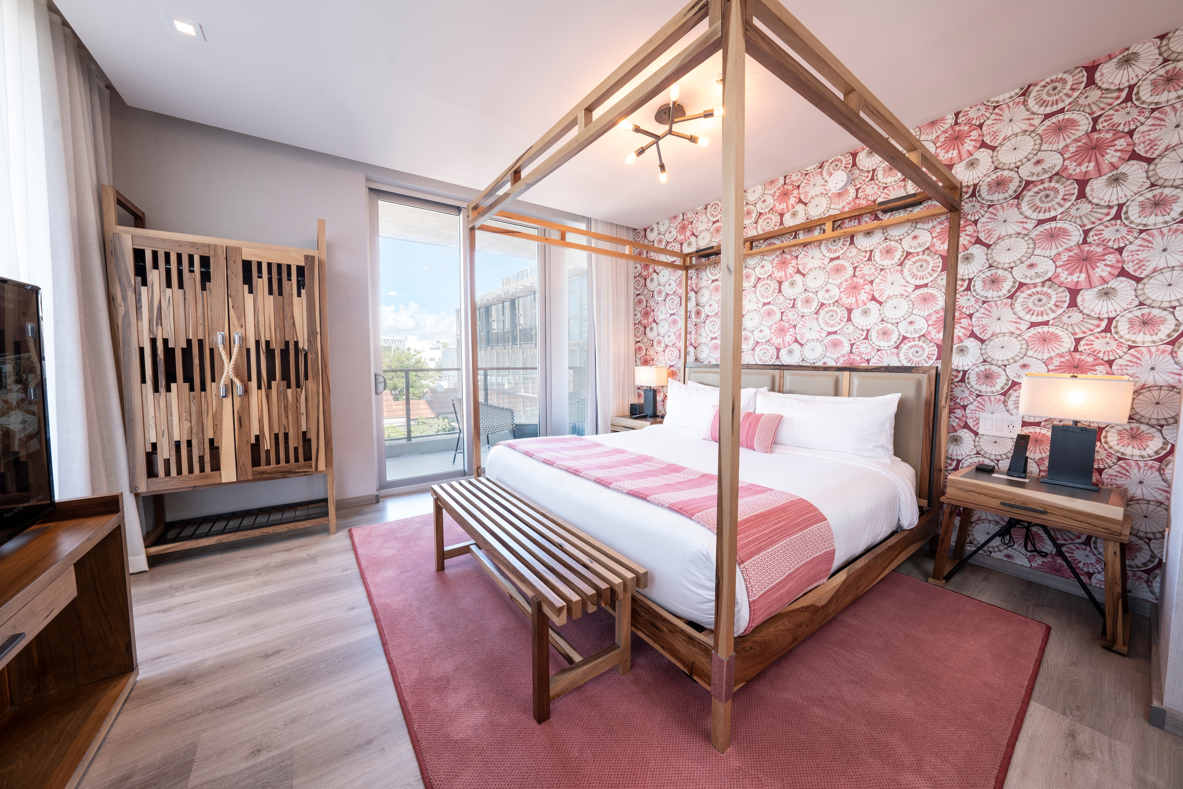 A wide view of a room with a four-poster bed, pink floral wallpaper, and a pink rug.