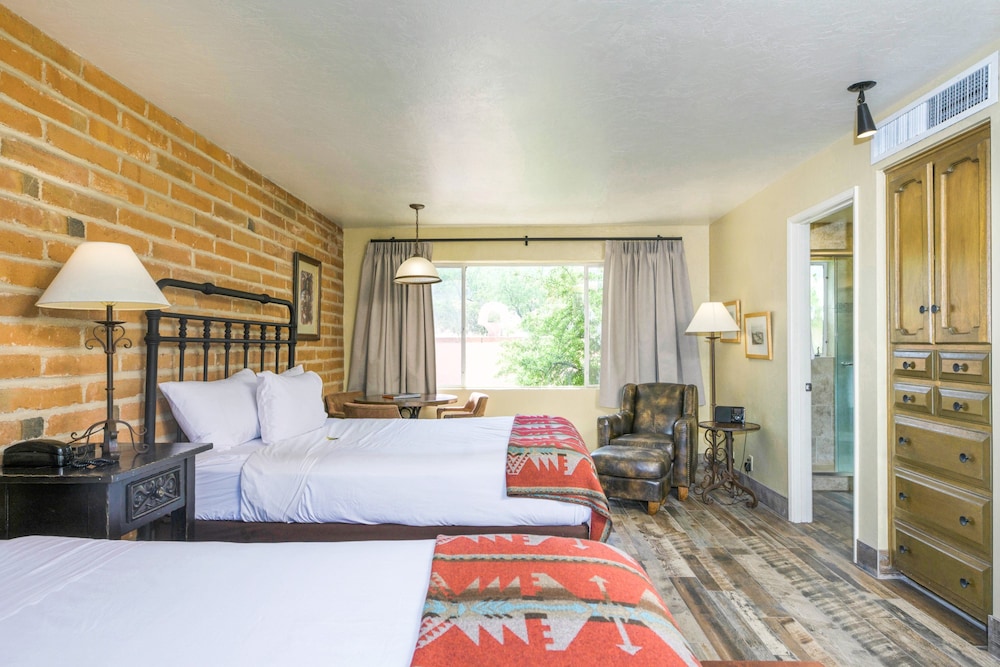 A wide view of a hotel room with two beds, a chair, and a window.