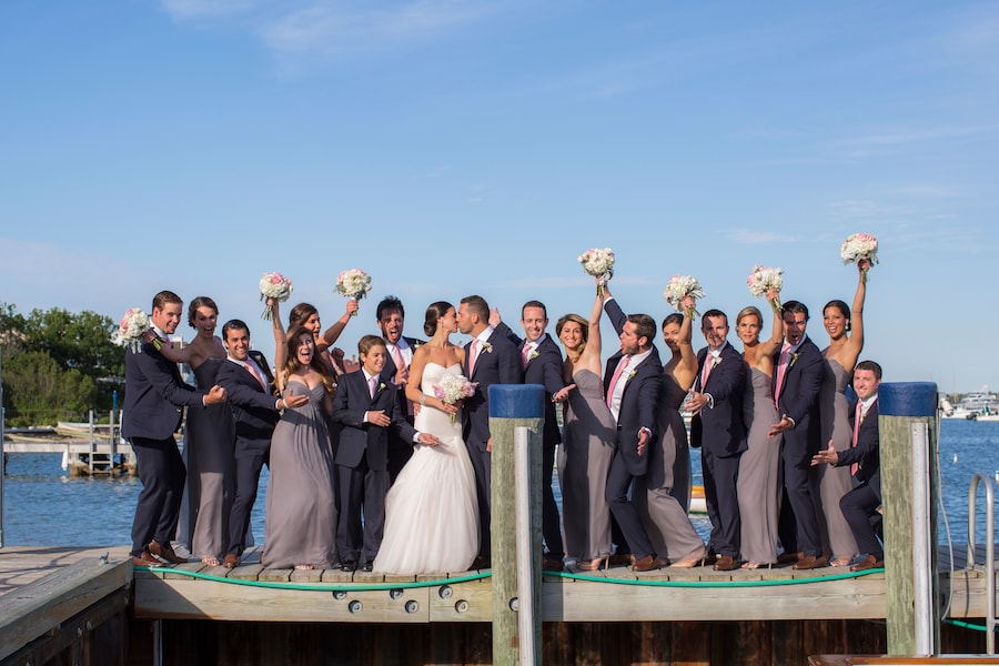 A group of people in formal attire standing on a dock by the water.
