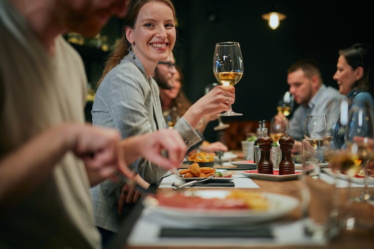 A group of people sitting at a table with wine and food