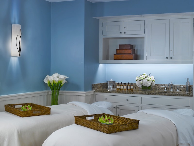 A serene spa room with twin beds, blue walls, and wicker trays on the beds.