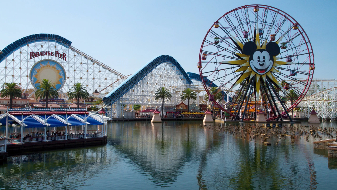 A scenic view of Paradise Pier and a Mickey Mouse-themed Ferris wheel near a body of water.